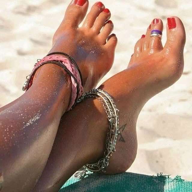 Pieds de femme sur la plage avec vernis rouge, chevillères et bague d'orteil
